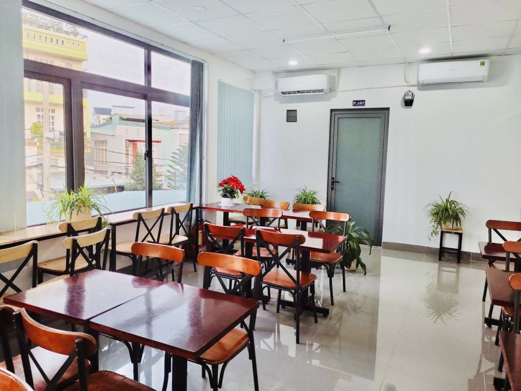 Phòng sinh hoạt chung với bàn ghế gỗ, cây xanh và cửa kính lớn
